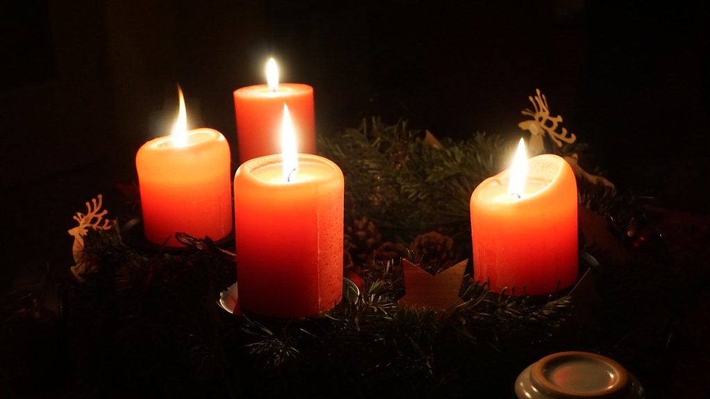Adventskranz mit vier brennenden Kerzen in der Dunkelheit