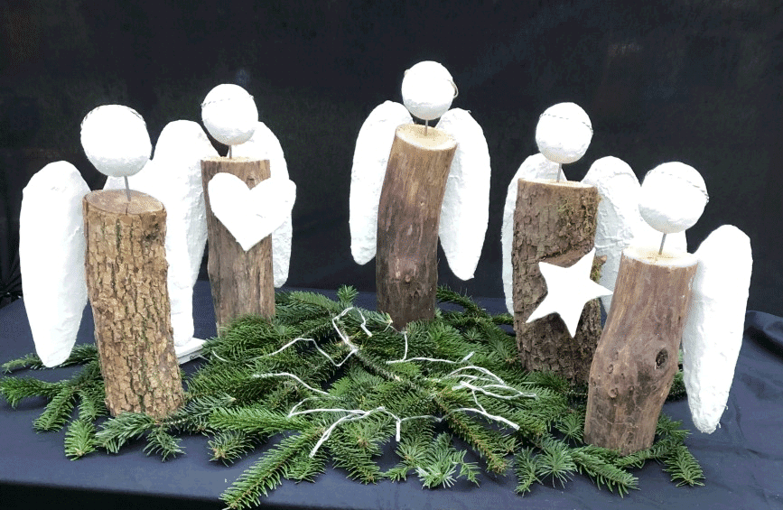 Gebastelte Engel, zum Teil aus Holz, stehen in einer Gruppe zusammen